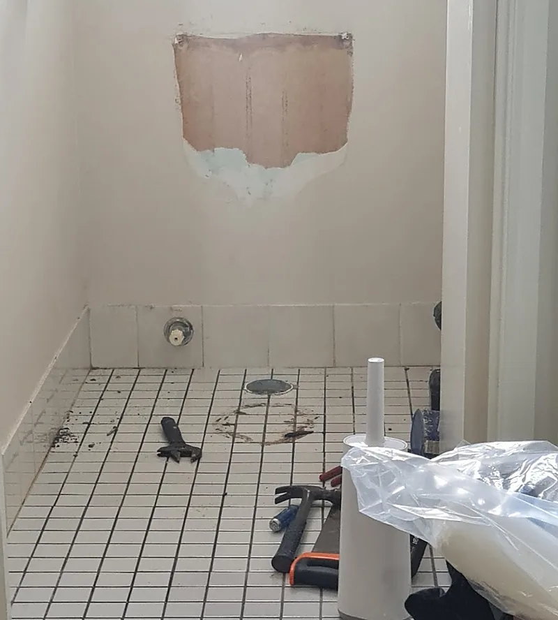 A toilet room mid-job: old suite removed, tools on the tiled floor and the wall opened up